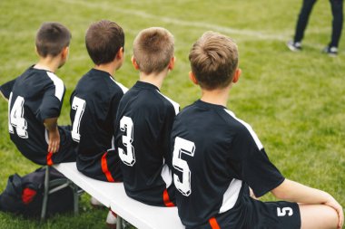 Spor takımındaki bir grup genç, beyaz yedek kulübesinde oturup oyun oynamak için fırsat kolluyor. Genç futbolcular için futbol maçı