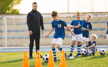 Futbol Eğitiminde Genç Çocuklar Grubu. Futbol koçu olan okul çocukları. Çocuk spor topuyla antrenman konilerine koşuyor. Yaz Kampı 'nda Erkek Eğitim Tekniği 