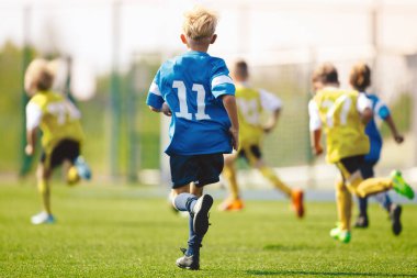 Futbol maçında oynayan çocuklar. Futbolcu gençler güneşli bir günde futbol topunu tekmeliyorlar. Okul çocukları için futbol turnuvası. Mavi ve sarı spor kıyafetli ilkokul çocukları.
