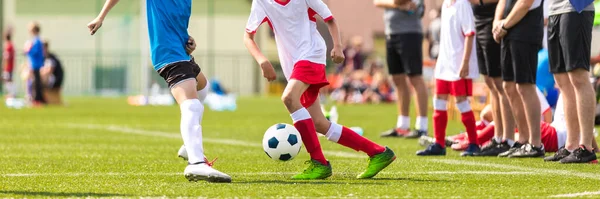 Kids in soccer running duel. Boys in two football teams running after classic soccer ball on school tournament. Horizontal sports background. Legs of young players on football pitch