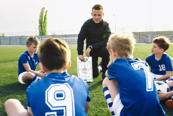 儿童足球训练营 年轻足球教练解释比赛规则和战术 策略使用白板 运动队与训练员坐在草皮上 — 图库照片