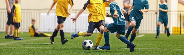 Horizontal image of football players kicking match. Boys in soccer duel. Kids in two football teams running after classic soccer ball. Horizontal sports background. Legs of young players on football pitch