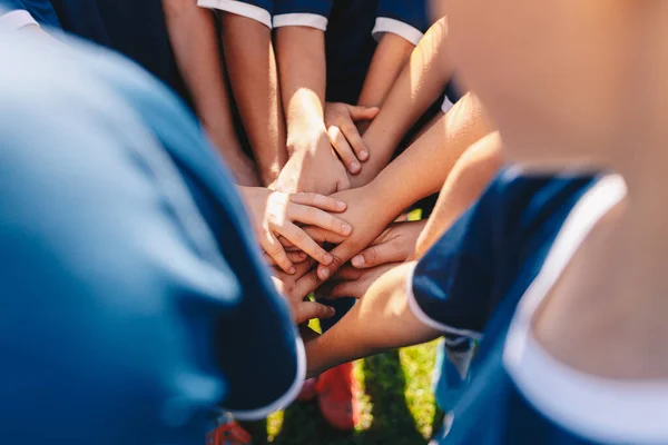 Group of happy children in sports team stacking hands outdoor in a summer day. Children team sports. Boys at sports camp stacking hands before a game. School age children in a team at the grass field
