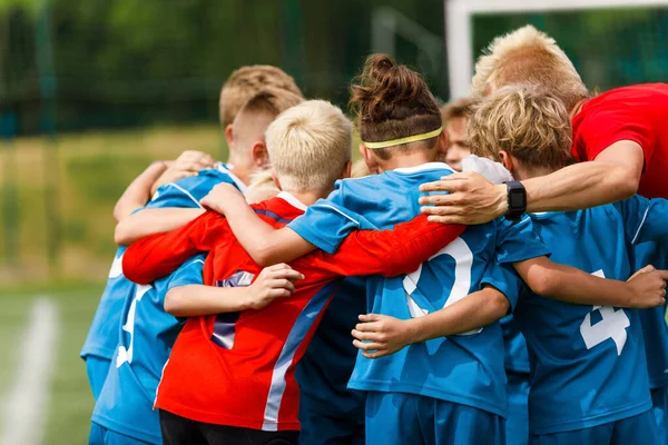 子供たちのコーチと一緒に群がってのグループ ユースサッカーチームの写真 子供たちはチームスポーツをする 幸せな男の子サッカー選手トーナメントキック 青と赤のジャージーシャツの男の子 — ストック写真