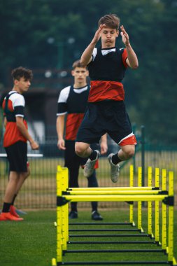 Sarı Eğitim Engelli Sırasından Atlayan Genç Adam. Spor Takımındaki Çocuklar Açık Hava Çeviklik Antrenmanında. Gençler Gençler Futbol Kulübü Çimen Eğitiminde Yetenek Geliştiriyor