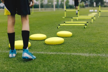 Futbol eğitim ekipmanları. Futbolcu antrenmana hazır. Oyuncu spor giyim ve futbol kramponları. Spor eğitim ekipmanları: denge yastıkları, engeller. Çimen futbol sahası