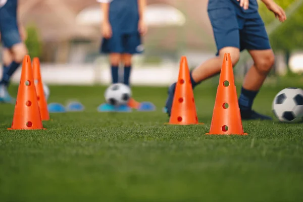 Players dribbling on football venue. Practice unit for football club. Boys running ball on grass training pitch. Red soccer training cones. Football class