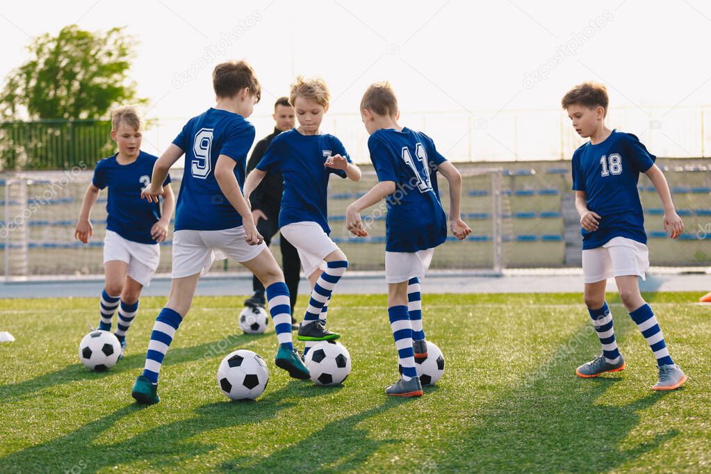 Group of children playing soccer on training session. Kids in football club wearing blue jersey shirts and soccer kits. Happy boys practicing football with coach on a sunny day