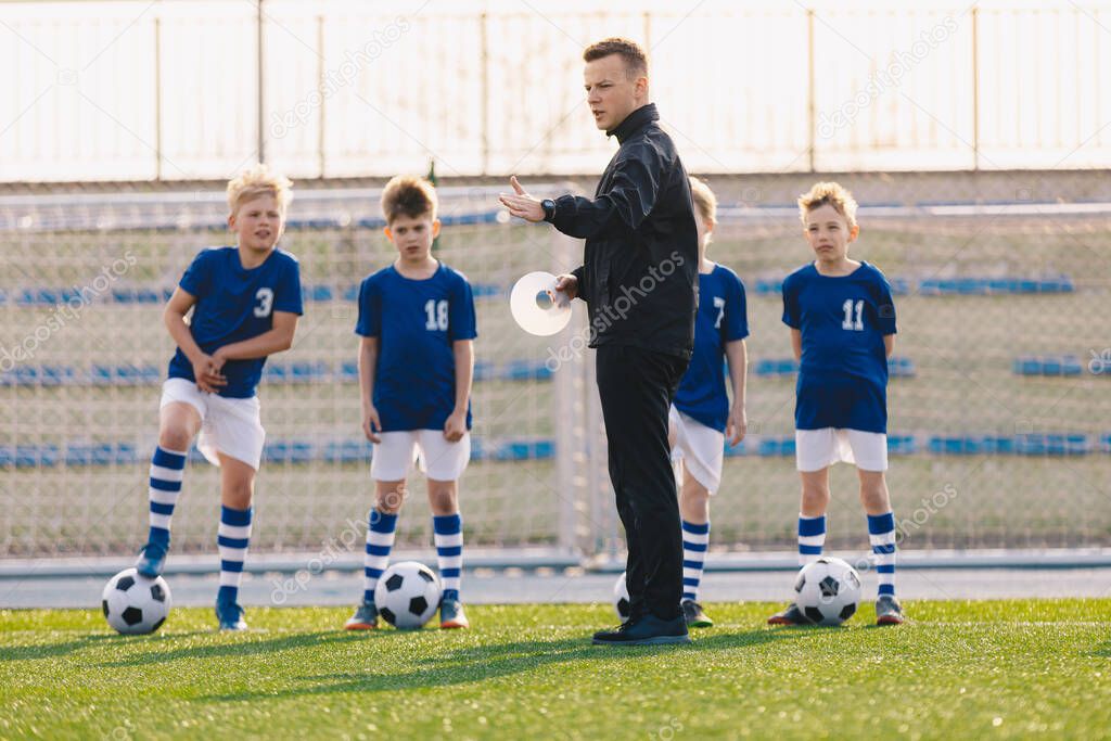 Young man soccer coach explaining training rules to group of children. Boys in football team on outdoor practice. School kid training soccer during physical education class