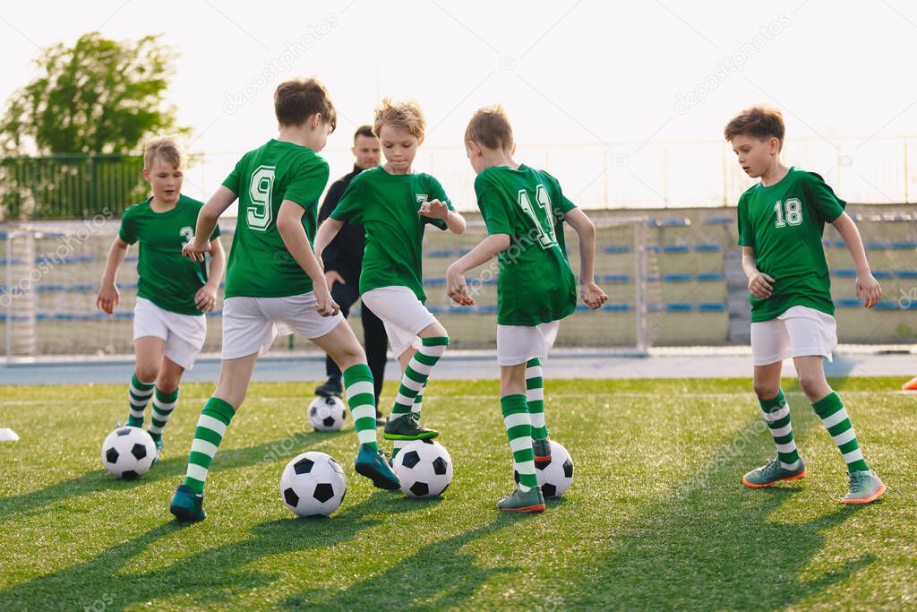 Group of children playing soccer on training session. Kids in football club wearing blue jersey shirts and soccer kits. Happy boys practicing football with coach on a sunny day