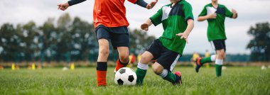 Oyuncular çimlerde futbol topunu tekmeliyor. Çocuklar futbol düellosunda. Bir grup okul çocuğu futbol sahasında spor yapıyor. Çocuklar futbol maçında yarışıyor