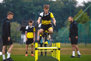 Genç Futbol Takımı antrenmanda. Futbol Kulübü 'nde Dayanıklılık Çalışması yapan Genç Çocuklar. Engelli engellerin üzerinden atlayan genç çocuk. Antrenman sahasında Genç Erkekler Spor Takımı. Gençlik Futbol Okulu
