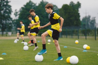 Teenage Boys Sports in a Row 'da eğitim görüyor. Genç Çocuklar için Futbol Yaz Kampı. Antrenmandaki Futbol Oyuncuları 'nız kutlu olsun. Gençlik Takımı Turf Pitch 'te topları tekmeliyor. Ekipmanlı Futbol Eğitim İzi