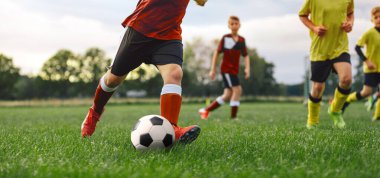Futbolcu topa vuruyor. Bir grup okul çocuğu çimlerin üzerinde futbol oynuyor.