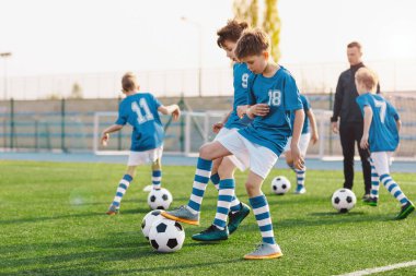 Çocuklar futbol antrenmanında oynuyor ve yarışıyor. Okul spor sahasında top tekmeleyen mutlu çocuklar.