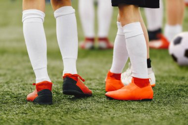 Yapay çim tarlasında kırmızı kramponlu futbol oyuncularının bacakları. Antrenman grubundaki futbol çocukları. Spor beyaz çoraplar. Arka planda klasik futbol topu