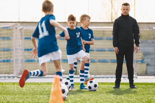 教孩子踢足球 年轻男子足球教练教练教练教练足球儿童营 身穿蓝色制服的足球少年跑得快 在训练球场上踢球 — 图库照片