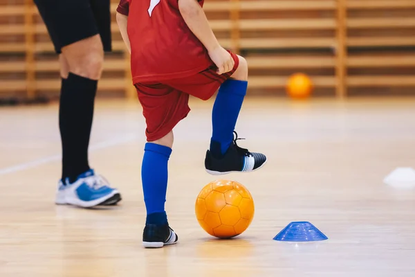 オレンジフットサルボールとサッカー服の男の子 コーチと屋内サッカートレーニングの子供 子供は木の床でフットサルをする コーチトレーナーとのフットサルスクールの練習 — ストック写真