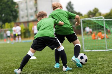 Futbol antrenmanında iki erkek çocuk yarışıyor. Okul futbol sahasında antrenman yapan mutlu çocuklar. Okul çocukları için yaz zamanı spor aktiviteleri