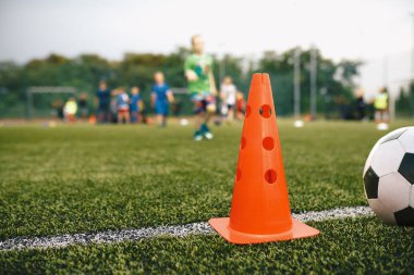 Football Grass Antrenman Sahası. Grass Pitch 'te futbol ekipmanı. Kırmızı Antrenman İşareti ve Futbol Topu. Arkaplanda Koşan Çocuklar Oyuncuları
