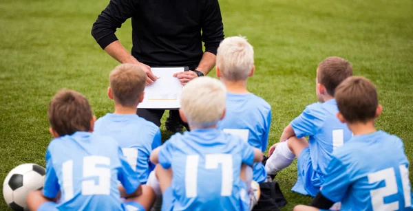 Football soccer match for children. Boys and coach sitting on green grass. — Stock Photo, Image