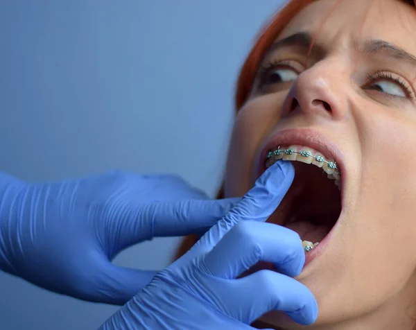 Doktor, kadının göğsündeki diş tellerini incelerken, kadın korku içinde ona bakıyor.