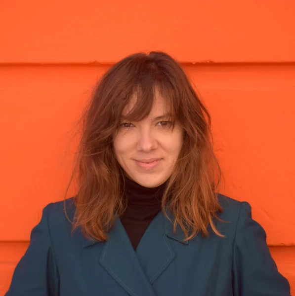 Önden turuncu arka planda çekilmiş mavi ceketli genç bir kadın.