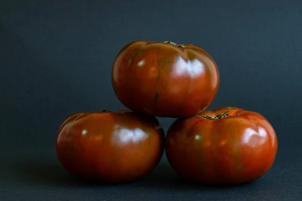 三个西红柿 一个在另外两个西红柿之上 在健康食品的黑色背景概念上形成一个三角形 — 图库照片