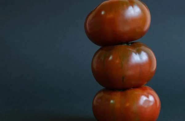 Üç domates üst üste dikey olarak siyah bir zemin üzerinde ve solda yazı için boşluk var..