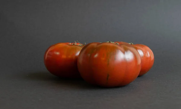 Siyah bir zemin üzerinde sarmaşığa yerleştirilmiş üç domates.