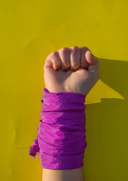 Kadın yumruğu, kadın hakları için, sarı arka planda ve mor atkıyla savaşmak üzere kaldırılır..