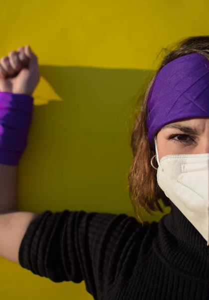 Kendini covid 19 'dan korumak için maskeli genç bir kadın. Feminist mücadelenin lehine mor atkı..
