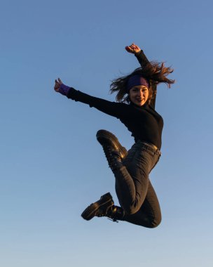 Siyah giysili ve çizmeli genç bir kadın mutlu bir şekilde zıplayıp duruyor. Mutluluk kavramı