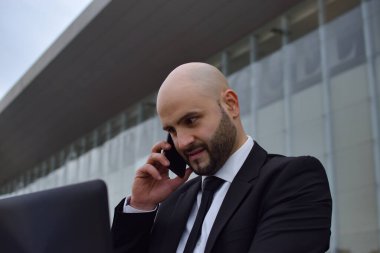 İş adamı dizüstü bilgisayarına bakarken telefonda konuşuyor.