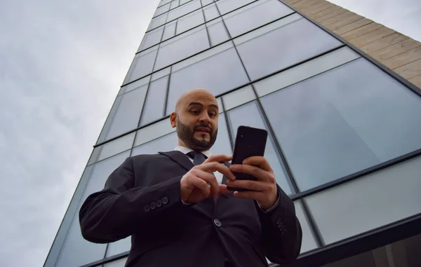 İş adamı arka planda gökdelenlerle cep telefonuna bakıyor. Finans kavramı.