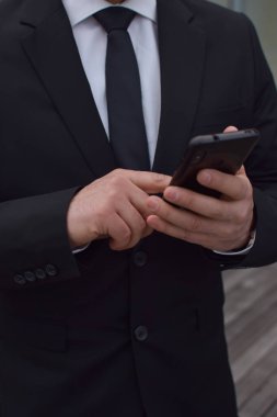 Beyaz adamın elleri takım elbise giymiş bir cep telefonuyla etkileşime girer. Herhangi birinin düşüncesi.