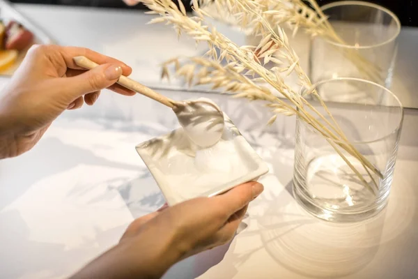 Genç bir kadının elleri bir kaşık kremayla kıpırdıyor. Çerçevede ev yapımı kozmetikler için birçok malzeme var..