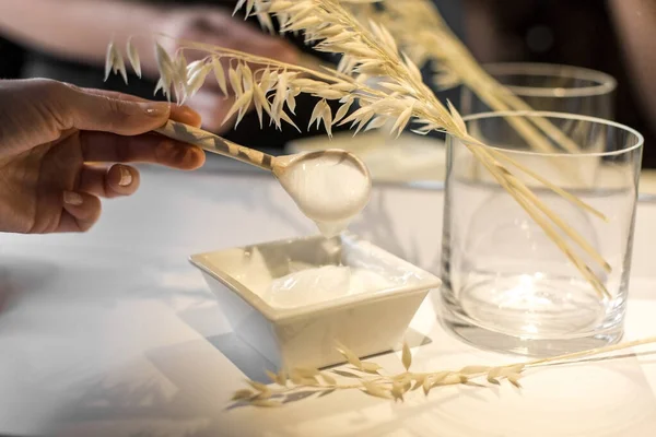 Genç bir kadının elleri bir kaşık kremayla kıpırdıyor. Çerçevede ev yapımı kozmetikler için birçok malzeme var..