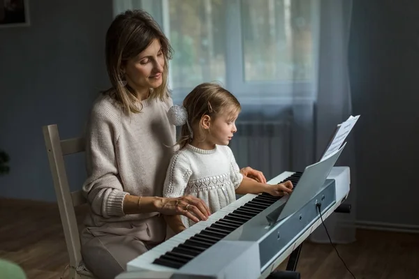 Studying music, mom and daughter are studying synthesizer. Keyboard game. Music lessons