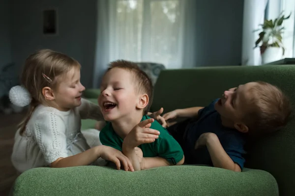 Tres hermosos niños y divertirse tumbado en el sofá en casa. —  Fotos de Stock