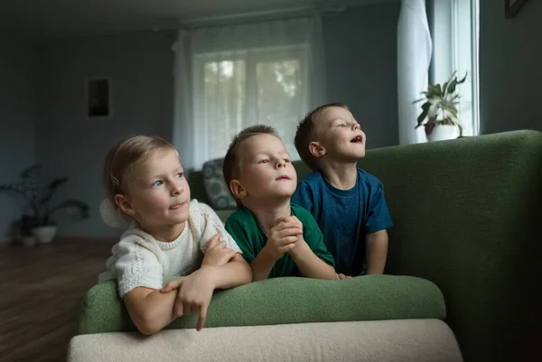 Piękne dzieci leżące na kanapie w domu i wyglądające przez okno. — Zdjęcie stockowe