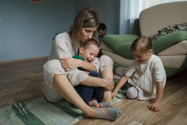 Mamá en casa sentada en el suelo se abraza y juega con los niños. —  Fotos de Stock