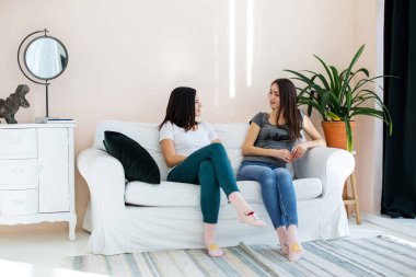 İki kız kanepede oturmuş birbirleriyle sohbet ediyorlar..