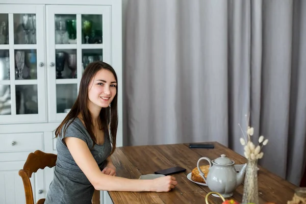 Esmer kız mutfaktaki ahşap masada oturuyor, çaydanlık ve çay.