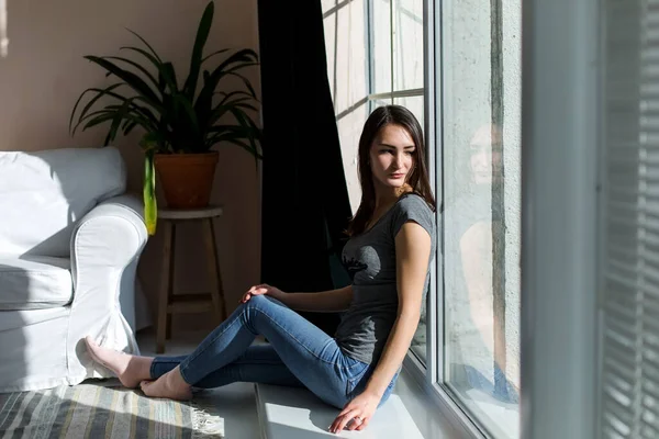 Kız yerde oturuyor, güneşin parladığı pencerenin yanında..