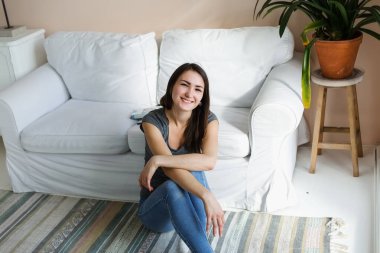 Kot pantolonlu kız, kanepenin yanında, parlak bir odada oturuyor..