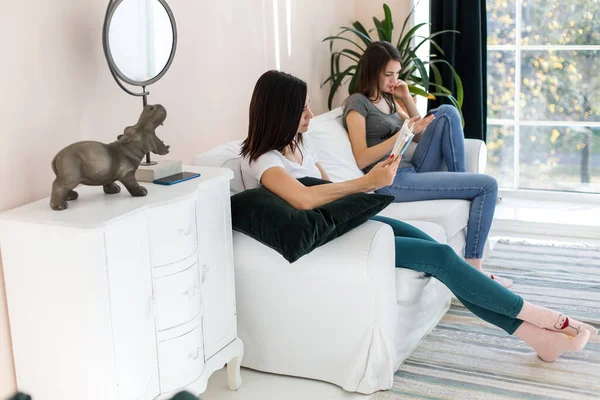 Kızlar kanepede oturmuş telefona ve kitaba bakıyorlar..