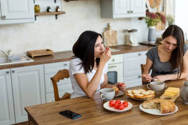 İki kız masada kek ve şekerle çay içiyor..