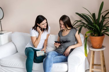 Kızlar kanepede oturmuş sohbet ediyor ve telefona bakıyorlar..