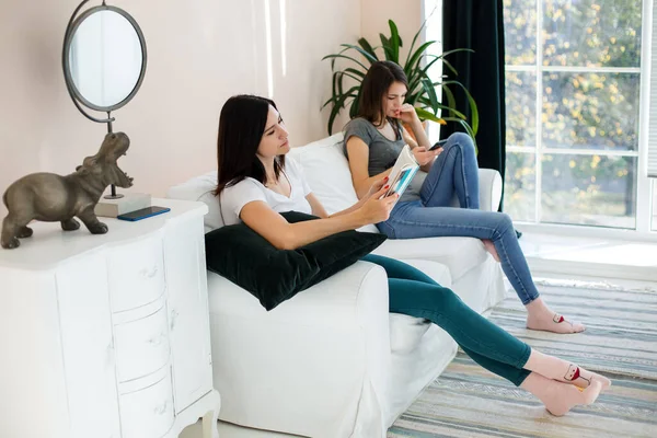 Kızlar kanepede oturmuş telefona ve kitaba bakıyorlar..